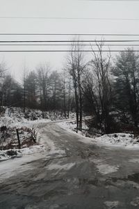 Snow covered road by trees against sky