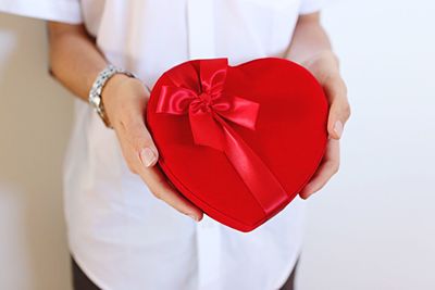 Midsection of woman holding heart shape present while standing against wall