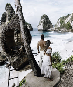 Rear view of friends on rock by sea against sky