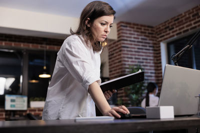 Side view of young woman using laptop while working in office