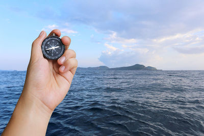 Cropped hand holding navigational compass against sky