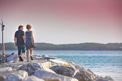 Rear view of couple walking on pier by sea against clear sky