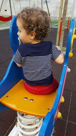 Rear view of baby girl sitting on outdoor play equipment at playground
