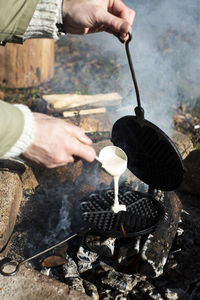 Hands of man pouring batter in waffle maker at bonfire