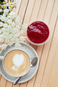 Cappuccino in a white ceramic cup with heart and raspberry jam dessert in a disposable cup 