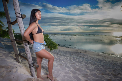 Young woman standing at beach against sky