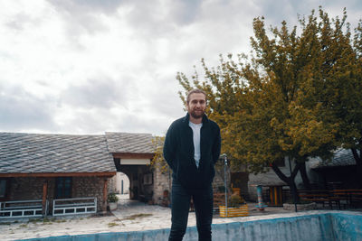 Portrait of smiling man standing by tree against sky