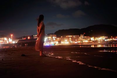 Rear view of woman standing at beach against sky at night