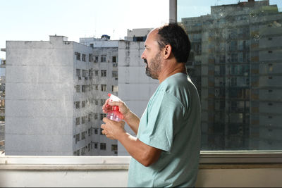 Middle-aged man at the window with the 70 alcohol spray to do the cleaning