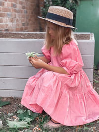 Full length of girl holding pink while sitting outdoors