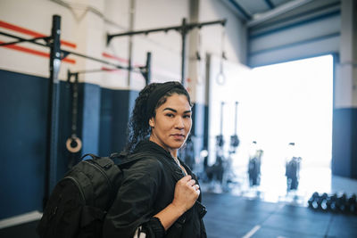 Confident female athlete with backpack in gym