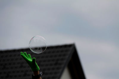 Cropped hand catching bubble against sky