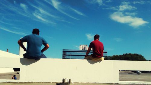 Rear view of shirtless men against blue sky