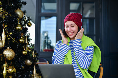 Shocked woman wearing knit hat while using laptop by tree during winter