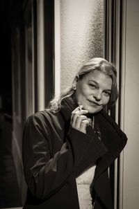 Portrait of smiling young woman smoking against wall