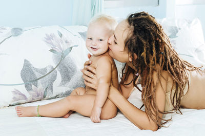 Mother kissing naked daughter on bed at home