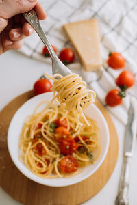 Spaghetti wrapped on a fork in the background of a portion of pasta with cherry tomatoes in a plate