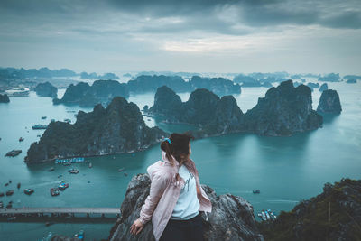 Woman sitting on rock while looking at sea against sky