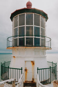 Exterior of lighthouse by sea against sky