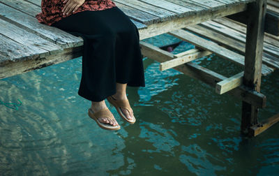 Low section of woman sitting on pier over lake