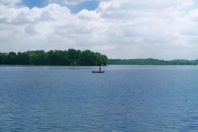 Scenic view of lake and fisherman against sky