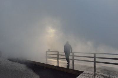 Rear view of man standing on pier against sky