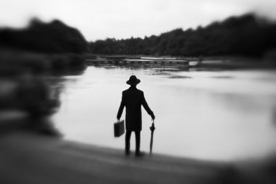 Rear view of man carrying suitcase and umbrella while standing on lakeshore