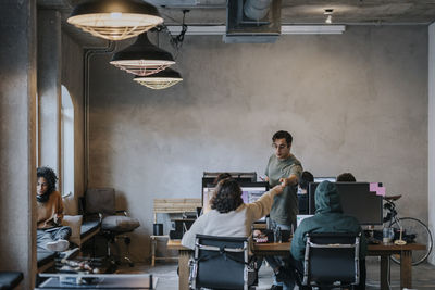 Multiracial female hacker giving pencil to male colleague by computers at desk in office