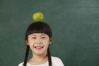Close-up portrait of girl with granny smith apple on head by blackboard