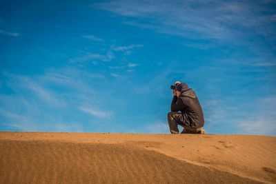 Side view of man photographing with digital camera in desert against sky