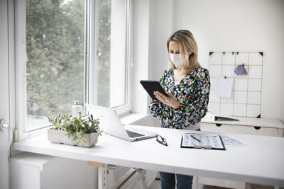 Businesswoman wearing mask using digital tablet at home