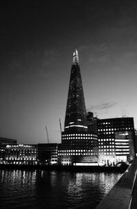 Illuminated buildings by river against sky at night