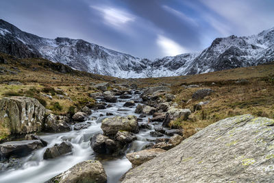 Scenic view of stream flowing amidst rocks against sky