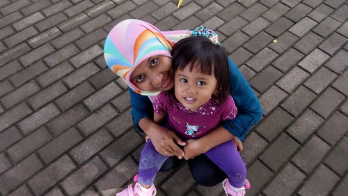 High angle portrait of mother with cute daughter crouching on street