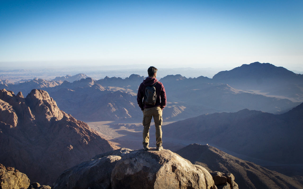 REAR VIEW OF MAN STANDING ON MOUNTAIN