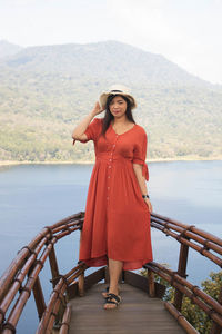 Portrait of smiling young woman standing on railing against mountain