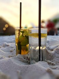 Close-up of drinks on sand at beach during sunset