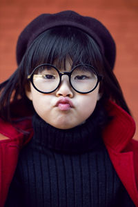 Korean girl in a red coat and cap and round glasses stands on red brick wall the street in autumn.