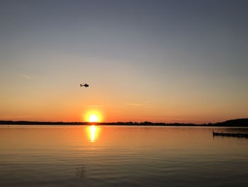 Silhouette helicopter flying over river against clear sky during sunset