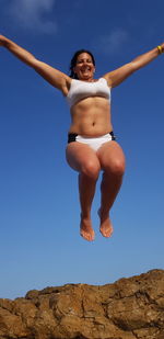 Low angle view of young woman jumping against clear blue sky