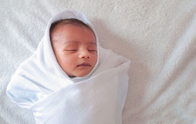 High angle view of baby boy wrapped in blanket sleeping on bed