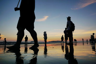 Silhouette people on beach against sky during sunset