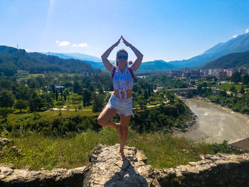 Full length of young woman with arms raised against sky