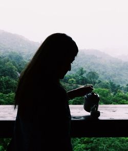 Side view of woman holding drink against mountain