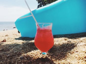 Close-up of drink on beach against blue sky