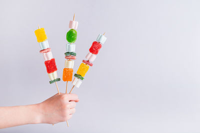 Cropped hand of person holding multi colored pencils against white background