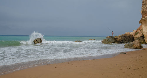 Scenic view of sea with man on rock against sky