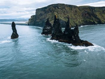 Scenic view of sea by mountain against sky