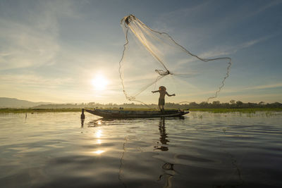 Man fishing in lake against sky during sunset
