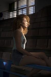 Portrait of young curly-haired woman sitting in a stadium with sunset light